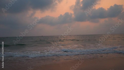 Wide angle slow motion shot of sea waves during the sunset at Candolim Beach in Goa, India. Clouds above the sea during the sunset. Beautiful beach sunset background. Summer holidays at beach concept. photo