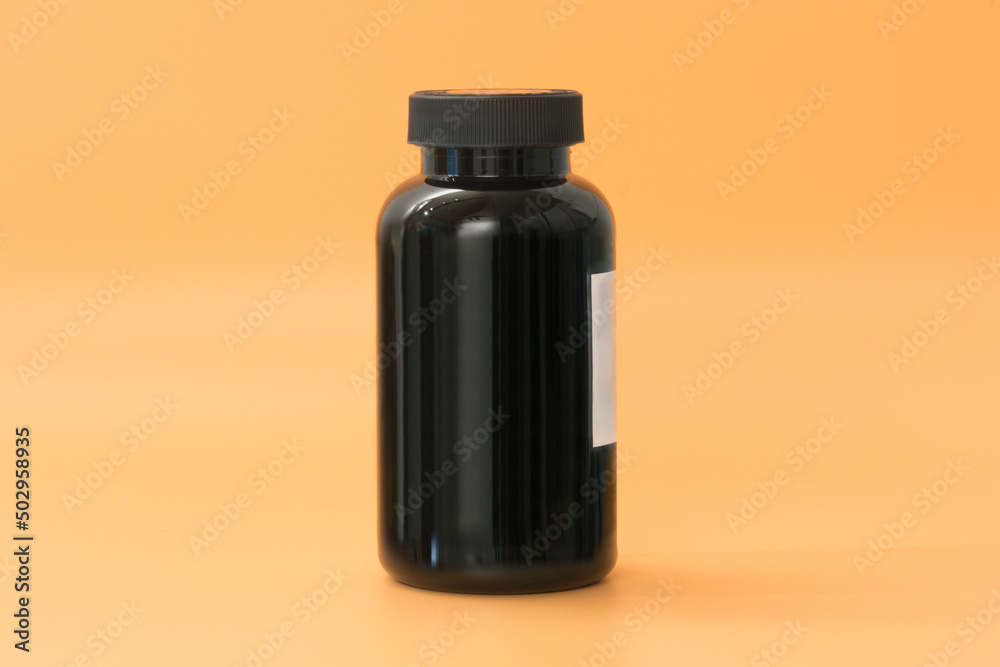 A tall black plastic supplement bottle stands on a yellow background. Workout. Vitamin. Pill. Pack. Prescription. Box. Healthy. Standing. Template A tall black plastic supplement bottle stands on a yellow background. Workout. Vitamin. Pill. Pack. Prescription. Box. Healthy. Standing. Template
