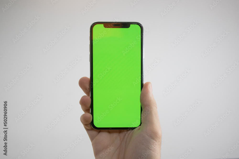 Holding an iPhone in hand. Green Screen on the phone. Mock-up of an iPhone. Apple product in hand. Vertical tilt of the phone. Holding an iPhone in hand. Green Screen on the phone. Mock-up of an iPhone. Apple product in hand. Vertical tilt of the phone.
