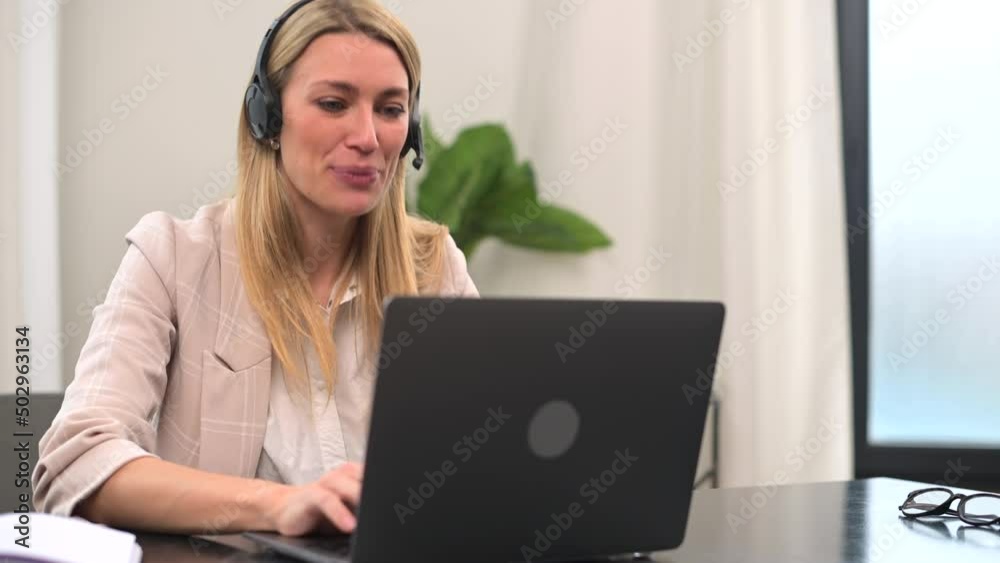 Young female call center operator with hands-free headset talking with client or customer in modern office. Concept of remote work. Businesswoman using laptop for online communication Young female call center operator with hands-free headset talking with client or customer in modern office. Concept of remote work. Businesswoman using laptop for online communication