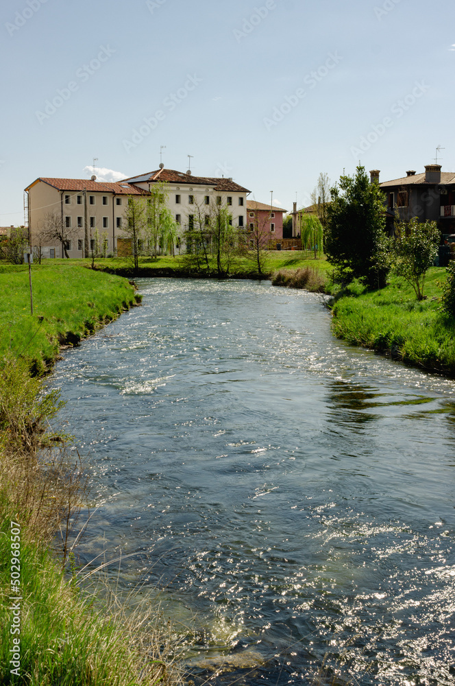 Meschio river flows between the houses. Vertical image. Province of Treviso, Italy.