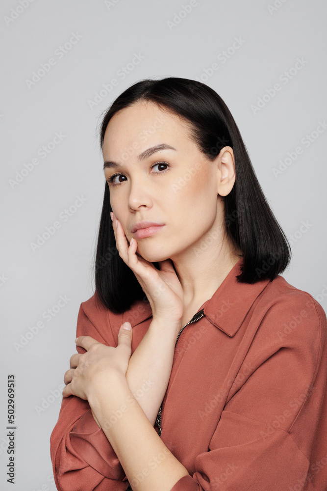 Portrait of serious young Asian woman with natural makeup touching own face against white background Portrait of serious young Asian woman with natural makeup touching own face against white background