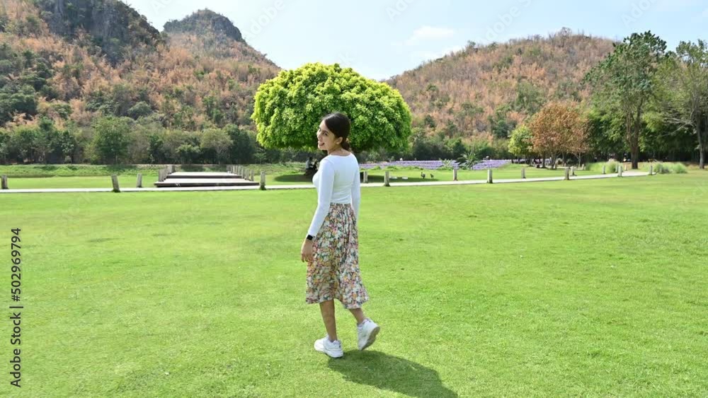 Cheerful young asian woman walking on grass into the big tree Cheerful young asian woman walking on grass into the big tree