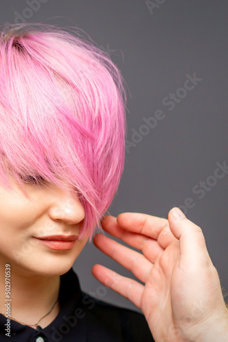 Hairdresser with hands is checking out and fixing the short pink hairstyle of the young white woman in a hair salon