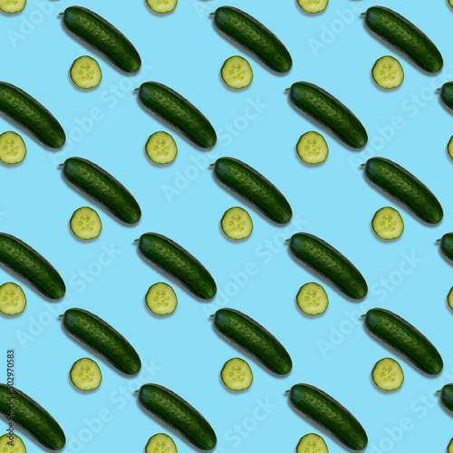 A pattern of fresh cucumber. Whole and sliced cucumbers on a blue background. View from above.