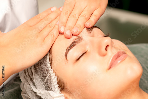 Head massage. Beautiful caucasian young white woman receiving a head and forehead massage with closed eyes in a spa salon