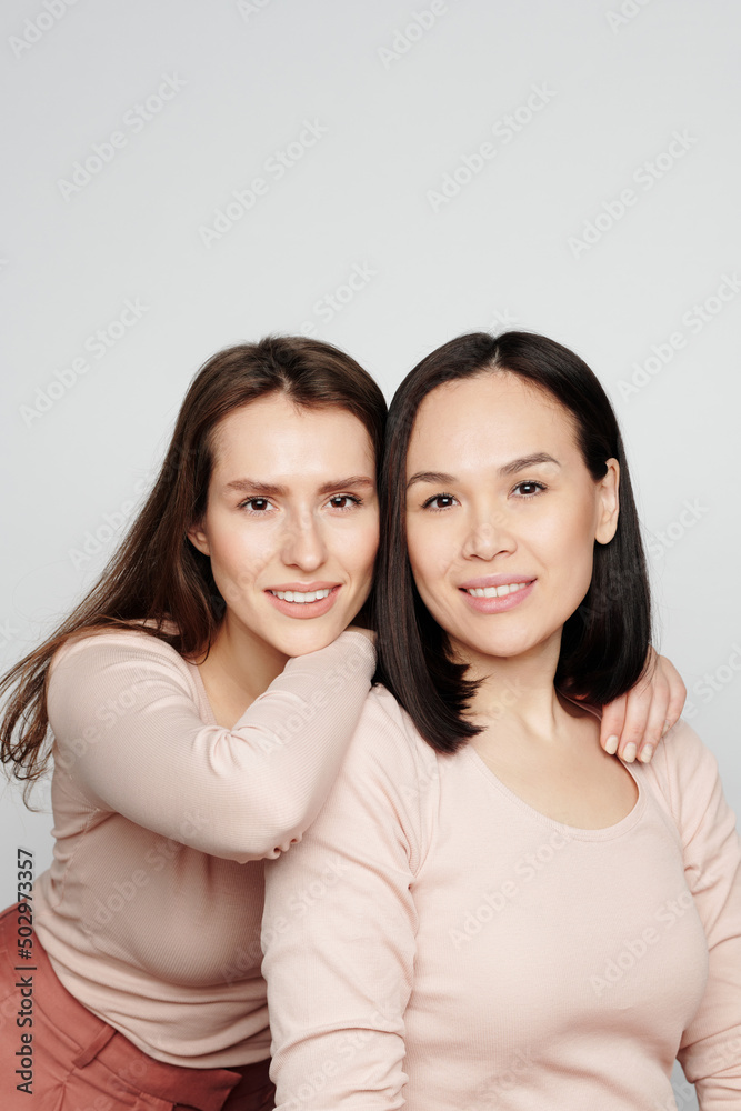 Portrait of smiling beautiful young Caucasian woman embracing Asian female friend behind back Portrait of smiling beautiful young Caucasian woman embracing Asian female friend behind back
