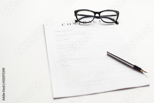 White table with paper contract detail and empty space to sign authorized signature, props with glasses and ink pen, copy space on the left