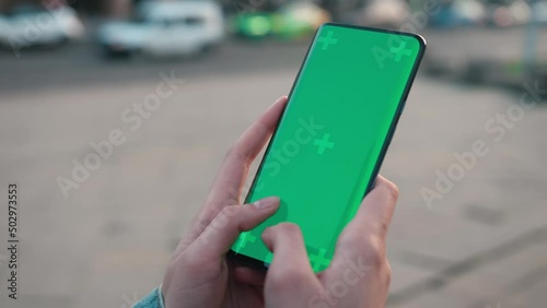 Lviv, Ukraine - May 6, 2022: Hands texting touch holding a mobile telephone with a vertical green screen outside chroma key smartphone technology cell phone street touch message display hand