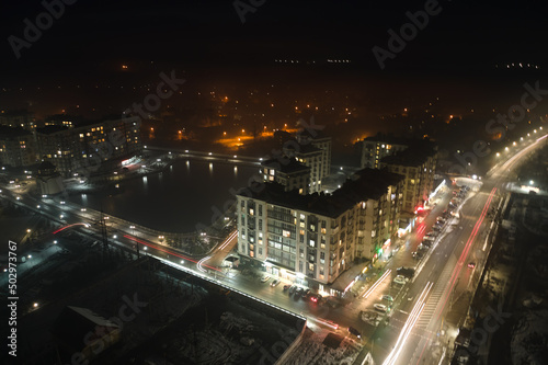 Aerial view of high rise apartment buildings and bright illuminated streets in city residential area at night. Dark urban landscape