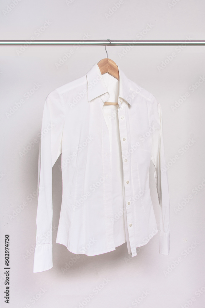 White shirt and wooden hanger on a rack after dry-cleaning on light background. Vertical photo. White shirt and wooden hanger on a rack after dry-cleaning on light background. Vertical photo.