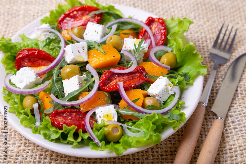 Warm salad with pumpkin, feta cheese, sun-dried tomatoes, olives, arugula and red onion. Close-up.