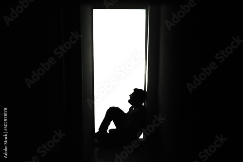 Konstfotografi Extreme silhouette shot: a sad, desperate man, crying while sitting alone on the floor near a door in his house, letting his bad feelings come out