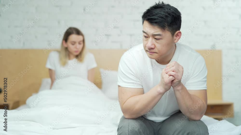Young unhappy family couple problem in bed. Upset young asian man sitting at home after quarrel. husband and wife are difficult in a relationship. Divorce, marriage, conflict, crisis, love concept Young unhappy family couple problem in bed. Upset young asian man sitting at home after quarrel. husband and wife are difficult in a relationship. Divorce, marriage, conflict, crisis, love concept
