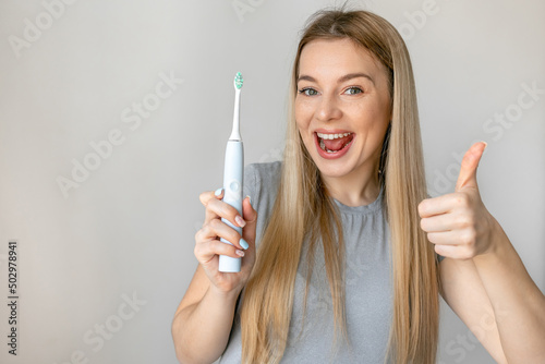 Happy woman holding electric toothbrush smiling happy and positive, thumb up doing excellent and approval sign