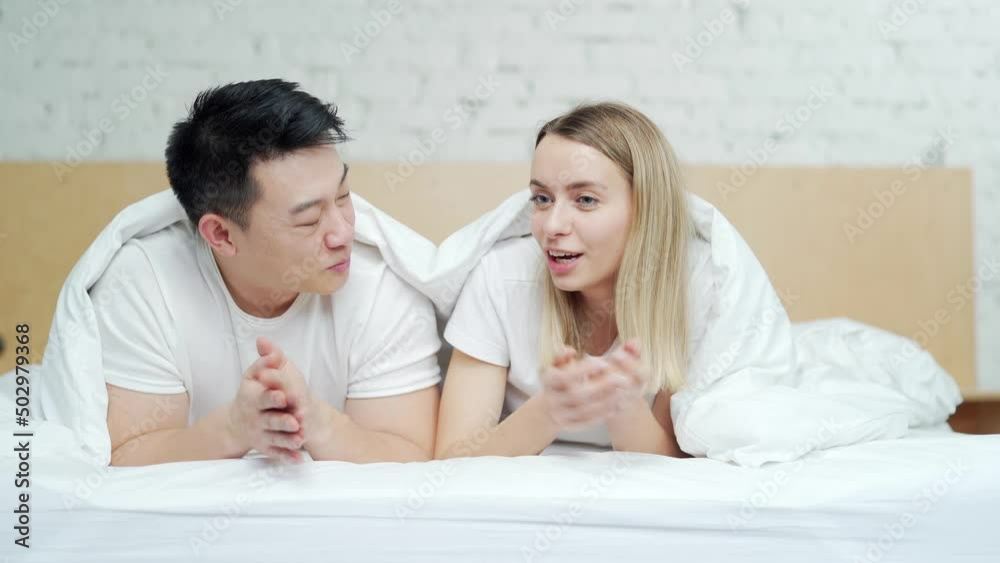 Happy young multiracial family lying together in bed. The couple spends leisure time together on weekends in the morning. Cheerful Asian husband and wife. Happiness and tenderness, people in love Happy young multiracial family lying together in bed. The couple spends leisure time together on weekends in the morning. Cheerful Asian husband and wife. Happiness and tenderness, people in love