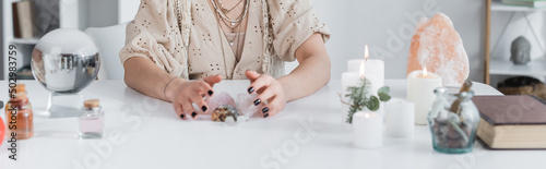 Cropped view of medium touching crystals near candles and magic orb at home, banner. photo