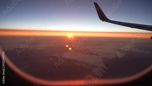 Looking out of window of flying at sunrise airplane. Point of view 4k video footage of amazing scenery during flight. Beautiful sunrise or sunset orange and blue sky outside of passanger air jet photo