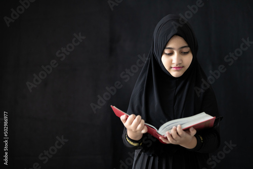 Photography muslim girl reading a holy book quran on black background