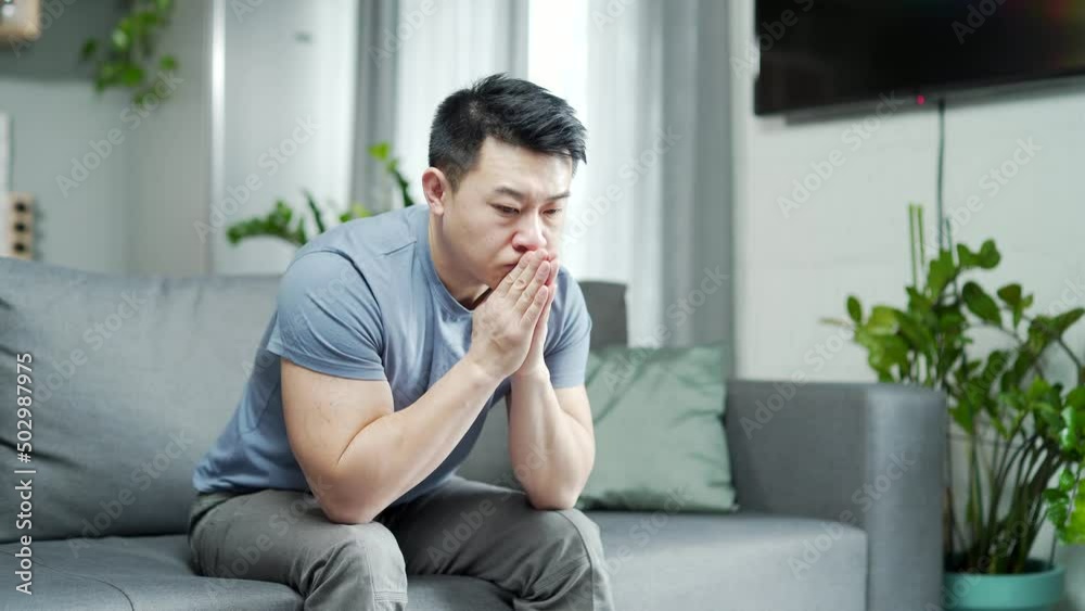 Young adult lonely depressed Asian man misses home. Sad Male sits on the couch and worries. guy indoors living room. stressed about problems in the family or work. incurable disease, negative thoughts Young adult lonely depressed Asian man misses home. Sad Male sits on the couch and worries. guy indoors living room. stressed about problems in the family or work. incurable disease, negative thoughts