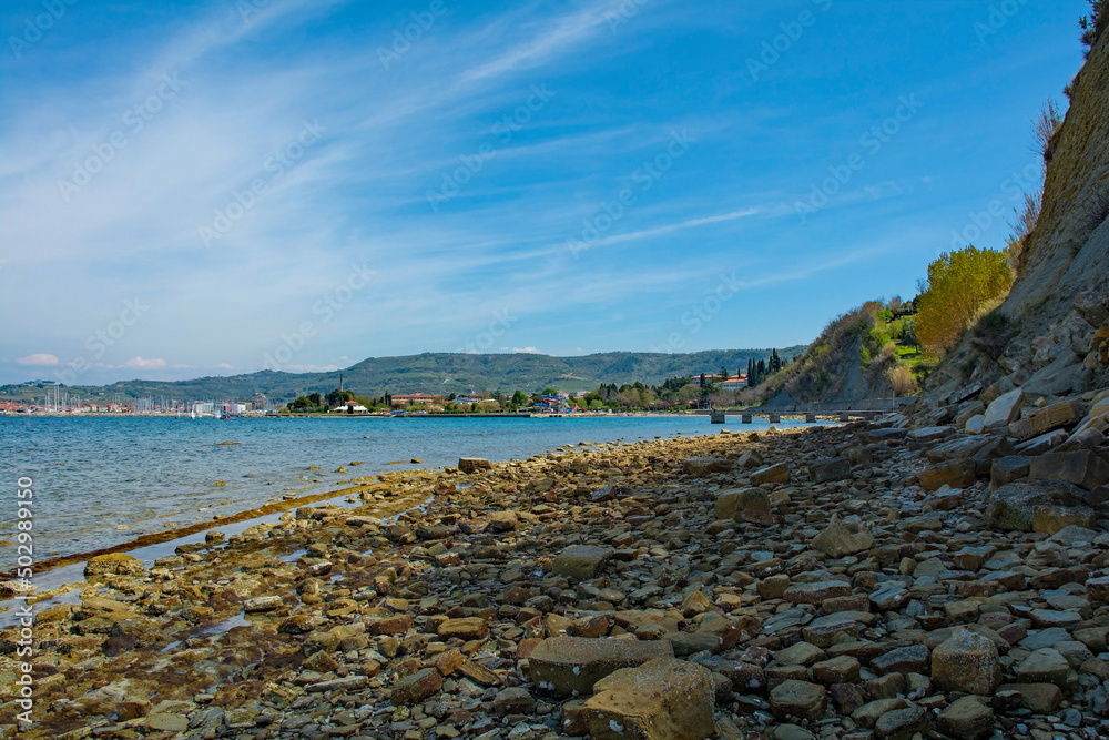A rocky beach on the Adriatic coast of Slovenia near Izola. The town of Izola is background left
