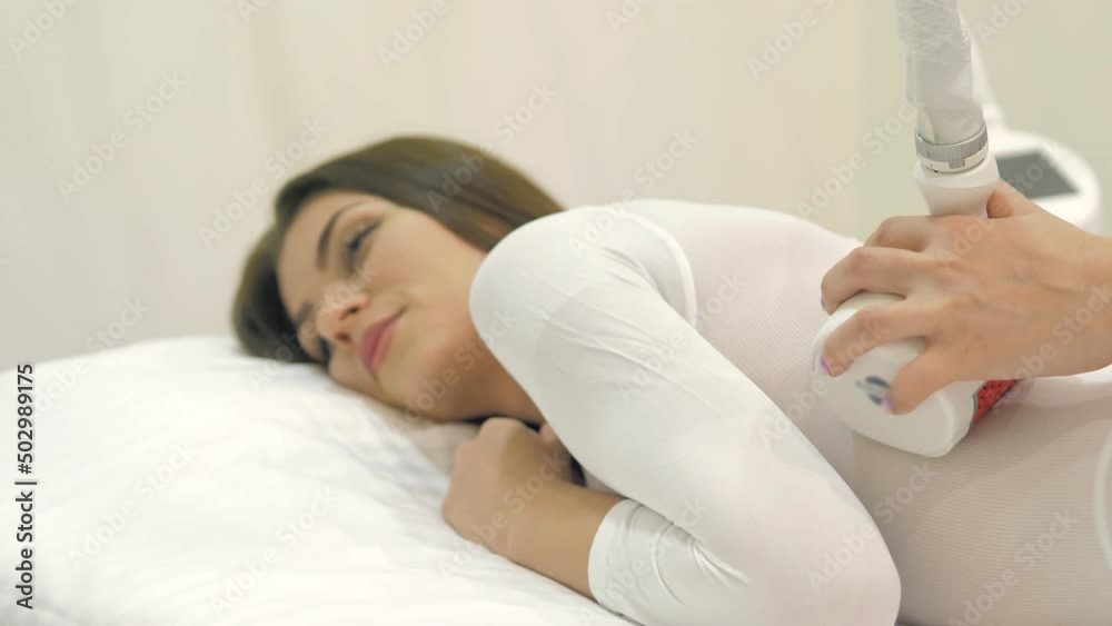 LPG massage in a beauty salon. A beautiful female client in a special white suit receiving an anti-cellulite massage in a beauty salon. A doctor manipulating a hardware cosmetology gadget. Body care LPG massage in a beauty salon. A beautiful female client in a special white suit receiving an anti-cellulite massage in a beauty salon. A doctor manipulating a hardware cosmetology gadget. Body care