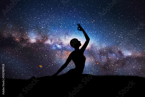 Yogi girl silhouette on grass. Woman doing yoga at night. Milky Way