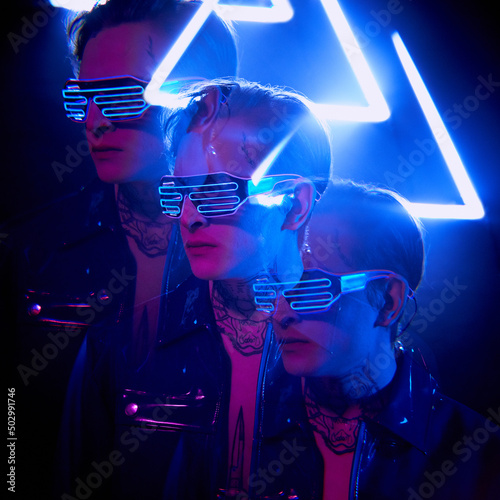 Serious young cyber man in neon goggles reflecting in 3D effect, neon light