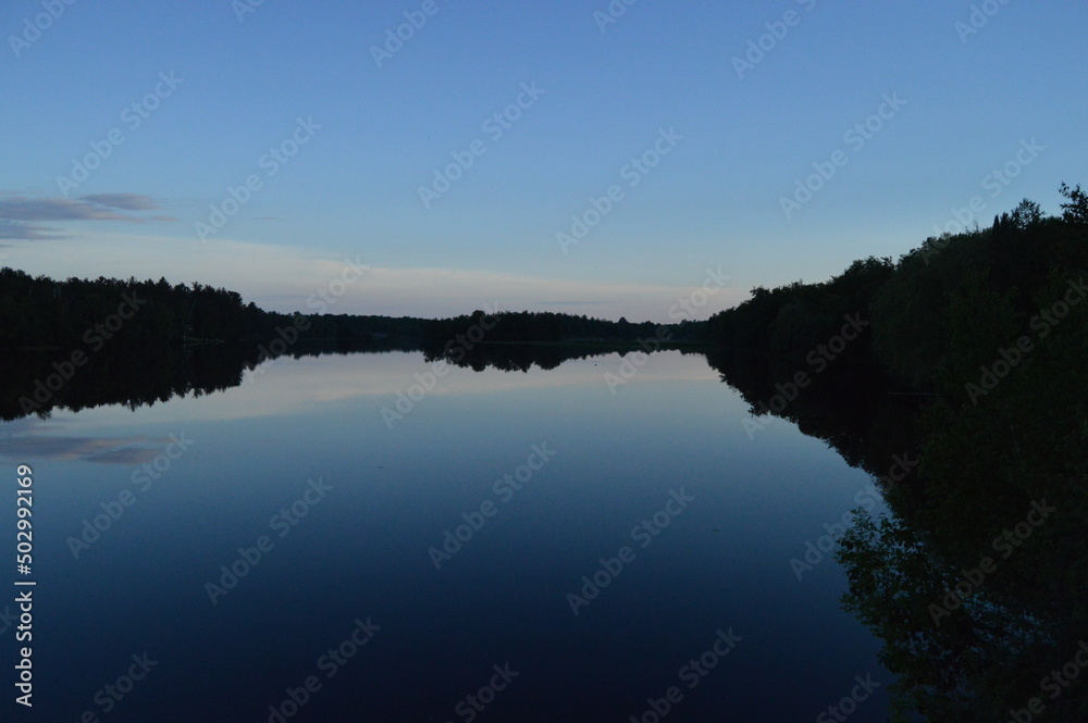 Soft blues and purples of post sunset sky reflect in the smooth peaceful lake surface of the Radisson Flowage in Northwest Wisconsin.