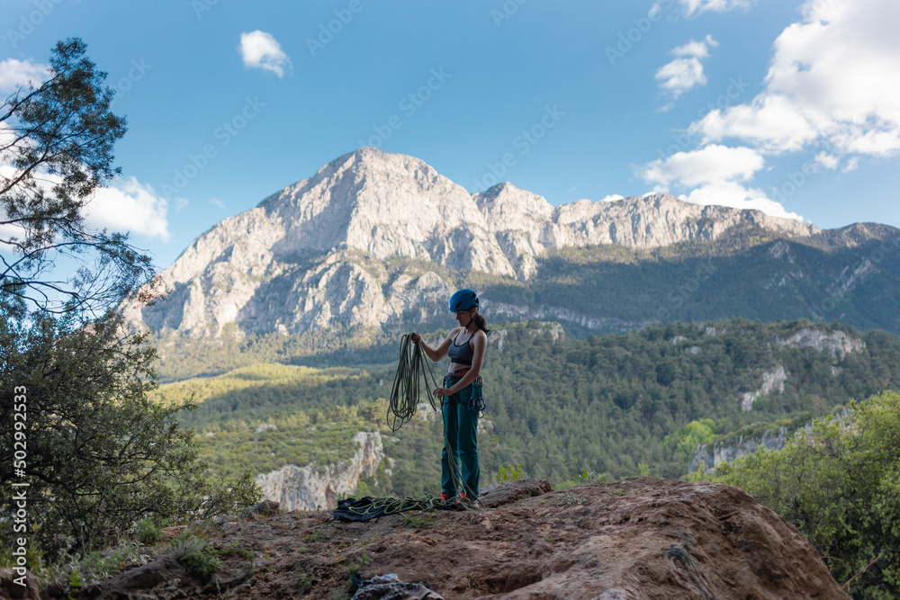 A woman in a helmet coils a rope against the background of a large mountain