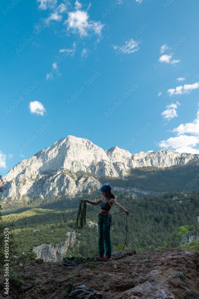A woman in a helmet coils a rope against the background of a large mountain