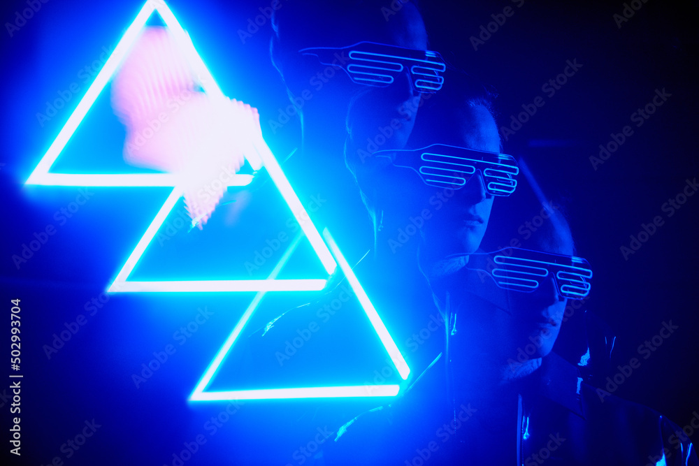 Cool boy in modern fashionable wire goggles standing in light of neon triangle sign Cool boy in modern fashionable wire goggles standing in light of neon triangle sign