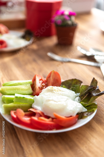 vegetables cucumbers, tomatoes, lettuce and poached eggs on a white plate on a wooden oak table. Concept on the theme of healthy eating