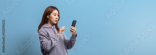 Portrait of beautiful Asian woman holding mobile phone on isolated background, portrait concept used for advertisement and signage, isolated over blue background, copy space.