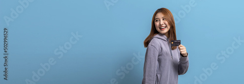 Portrait of Asian woman holding a credit card, credit card spending concept, online payment and general store with credit card, isolated over blue background, copy space