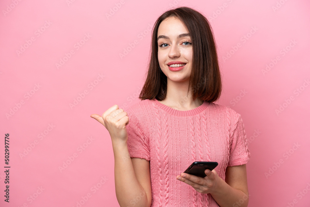 Young Ukrainian woman isolated on pink background using mobile phone and pointing to the lateral Young Ukrainian woman isolated on pink background using mobile phone and pointing to the lateral