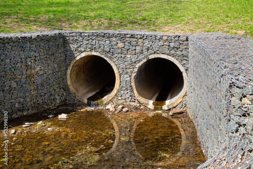 Картината върху платно The entrance to the concrete round collector for the river, stream with grass, sand and granite stones on the sides