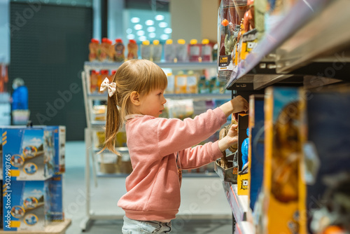 Little caucasian girl choosing a new toy in the big baby store. Big shelfs full of toys