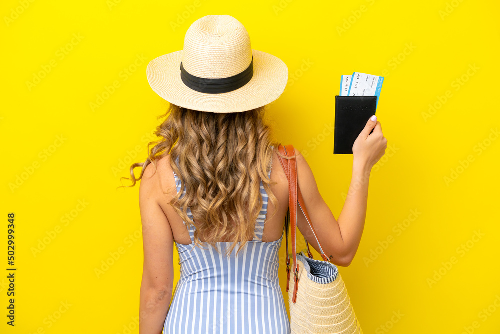 Young woman goes on vacation to the beach isolated on yellow background in back position Young woman goes on vacation to the beach isolated on yellow background in back position
