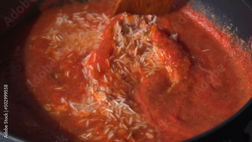 Jollof rice in a frying pan cooking. A traditional Nigerian dish of rice, tomatoes and spices.