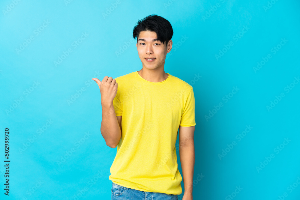 Young Chinese man isolated on blue background pointing to the side to present a product Young Chinese man isolated on blue background pointing to the side to present a product