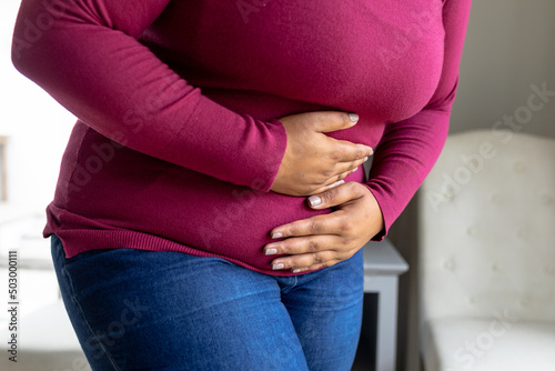 Midsection of african american mid adult woman with hands on stomach suffering from stomachache photo