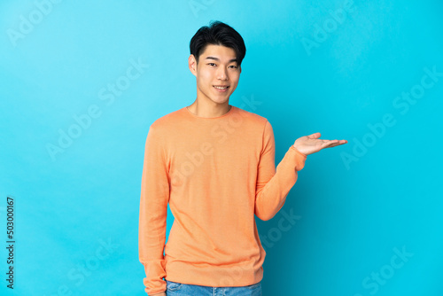 Cuadro en lienzo Young Chinese man isolated on blue background holding copyspace imaginary on the