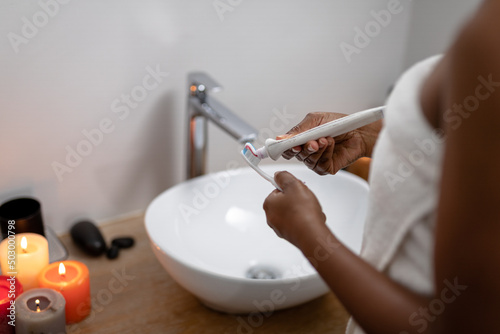 Midsection of african american mid adult woman applying toothpaste on brush in bathroom