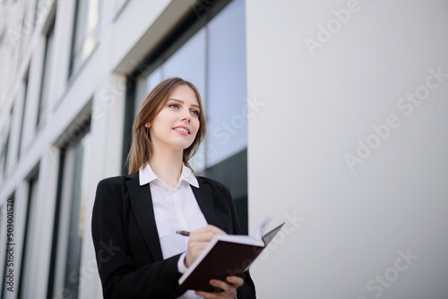 A beautiful woman is holding a notebook and a pen, dressed in business clothes.