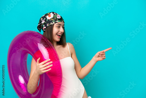 Young Ukrainian woman holding air mattress isolated on blue background pointing finger to the side and presenting a product