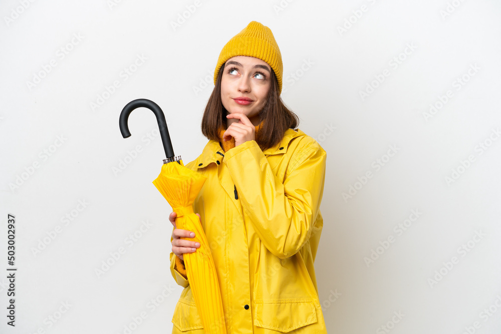 Young Ukrainian woman with rainproof coat and umbrella isolated on white background and looking up