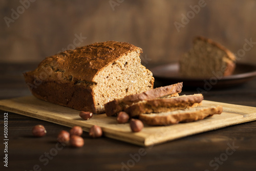 Homemade banana bread with hazelnuts on a cutting board on a rustic wooden background. Vegan pastries. Healthy breakfast. Selective focus.


