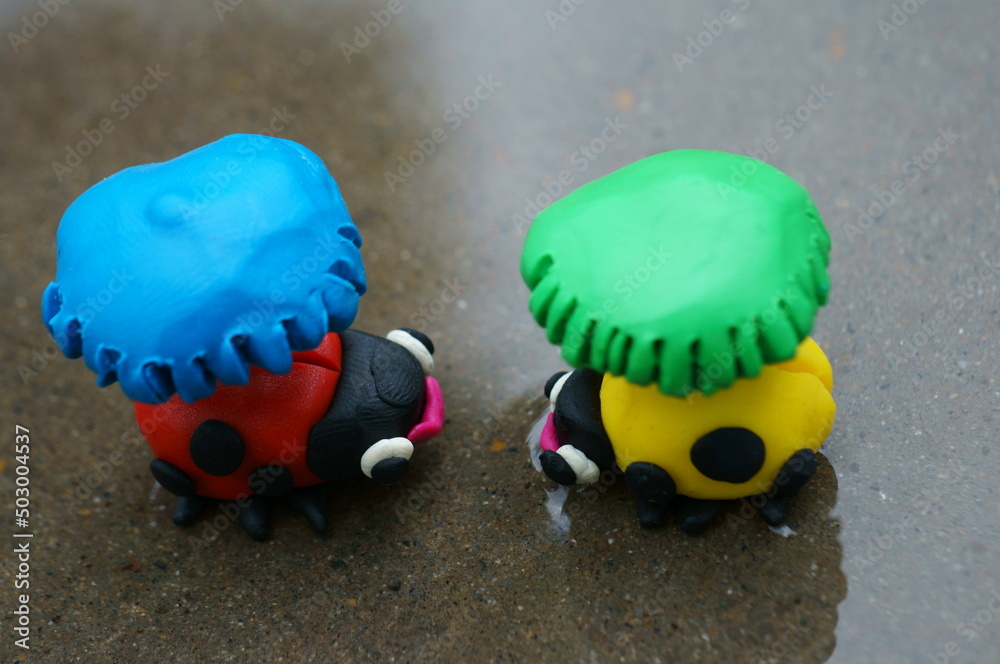 Obraz premium Figures of two ladybirds with umbrellas stand in a puddle.