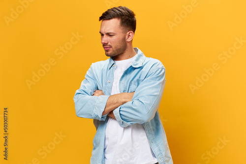 Sad frustrated tanned handsome man in blue basic t-shirt think about problem at work fold arms posing isolated on yellow studio background. Copy space Banner Mockup. People emotions Lifestyle concept